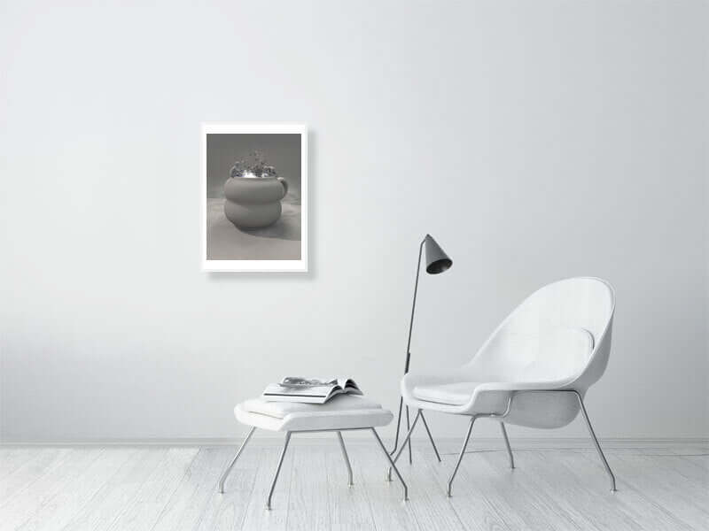 Modern living room with framed digital art print titled "Cup - Clay Mode" on wall. Minimalist decor with chair, footstool, and lamp.