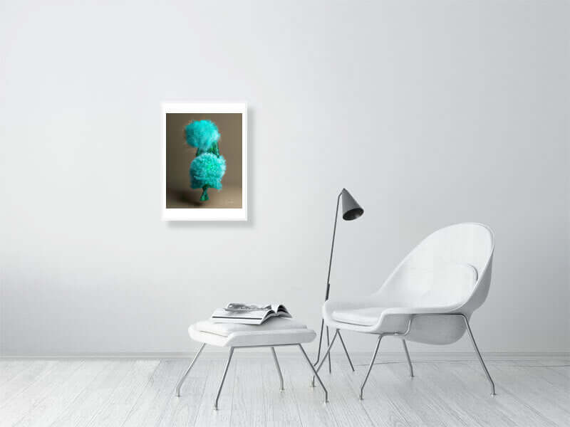 Modern living room with framed digital art print on wall, featuring trippy turquoise design. White chair, table with open book, and floor lamp.